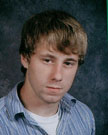 A young man with light brown hair, wearing a blue and white striped shirt, poses for a school portrait against a dark background.