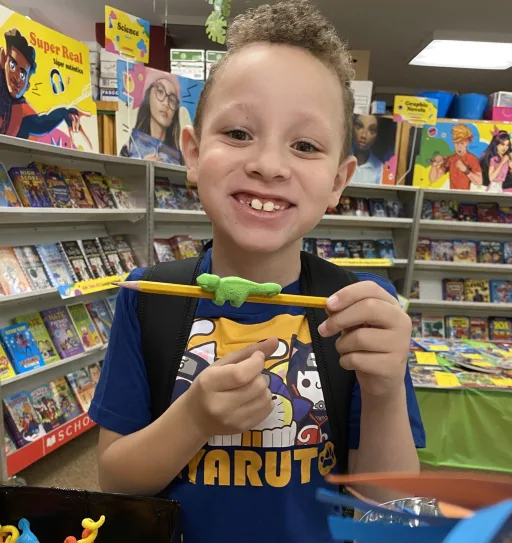 kid at the library holding a pencil with a clay dinopusure