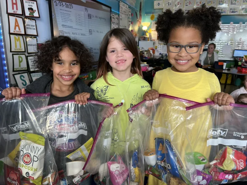 3 sutdents with big bags with snacks smiling