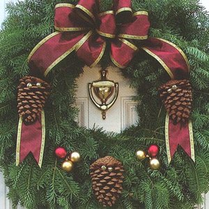 A festive green wreath adorned with pine cones, red and gold ornaments, and a large red bow, hanging on a door with a bell in the center.
