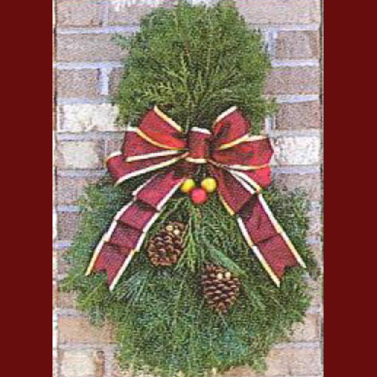 A festive green wreath adorned with a large red and gold bow, featuring two pine cones and colorful ornaments, hanging against a brick wall.