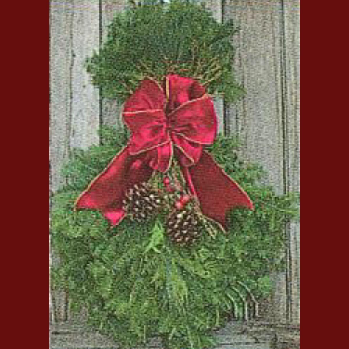 A festive green wreath adorned with a large red bow and pinecones, hanging against a wooden background.