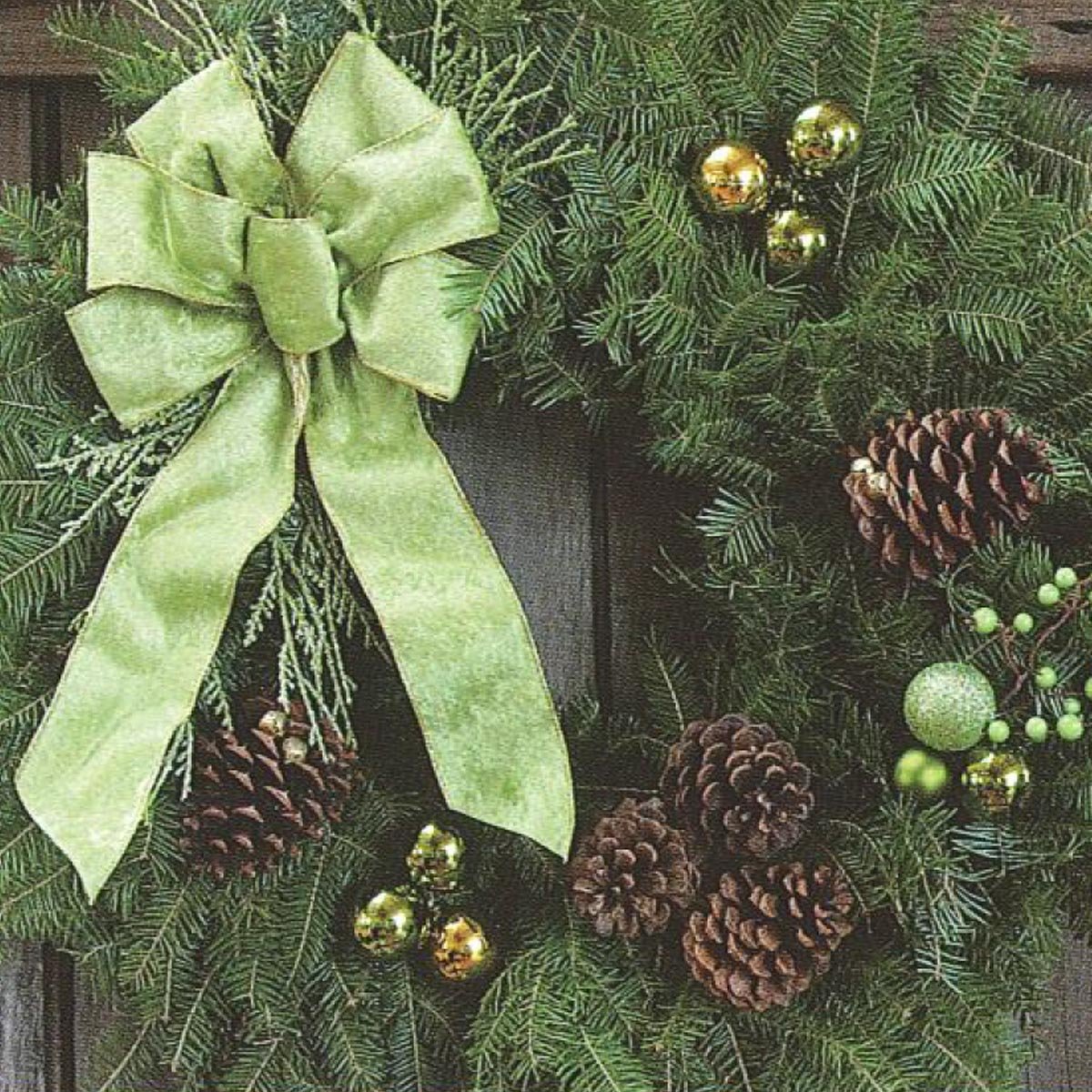 A decorative green wreath adorned with a large bow, pine cones, and shiny ornaments, set against a wooden background.