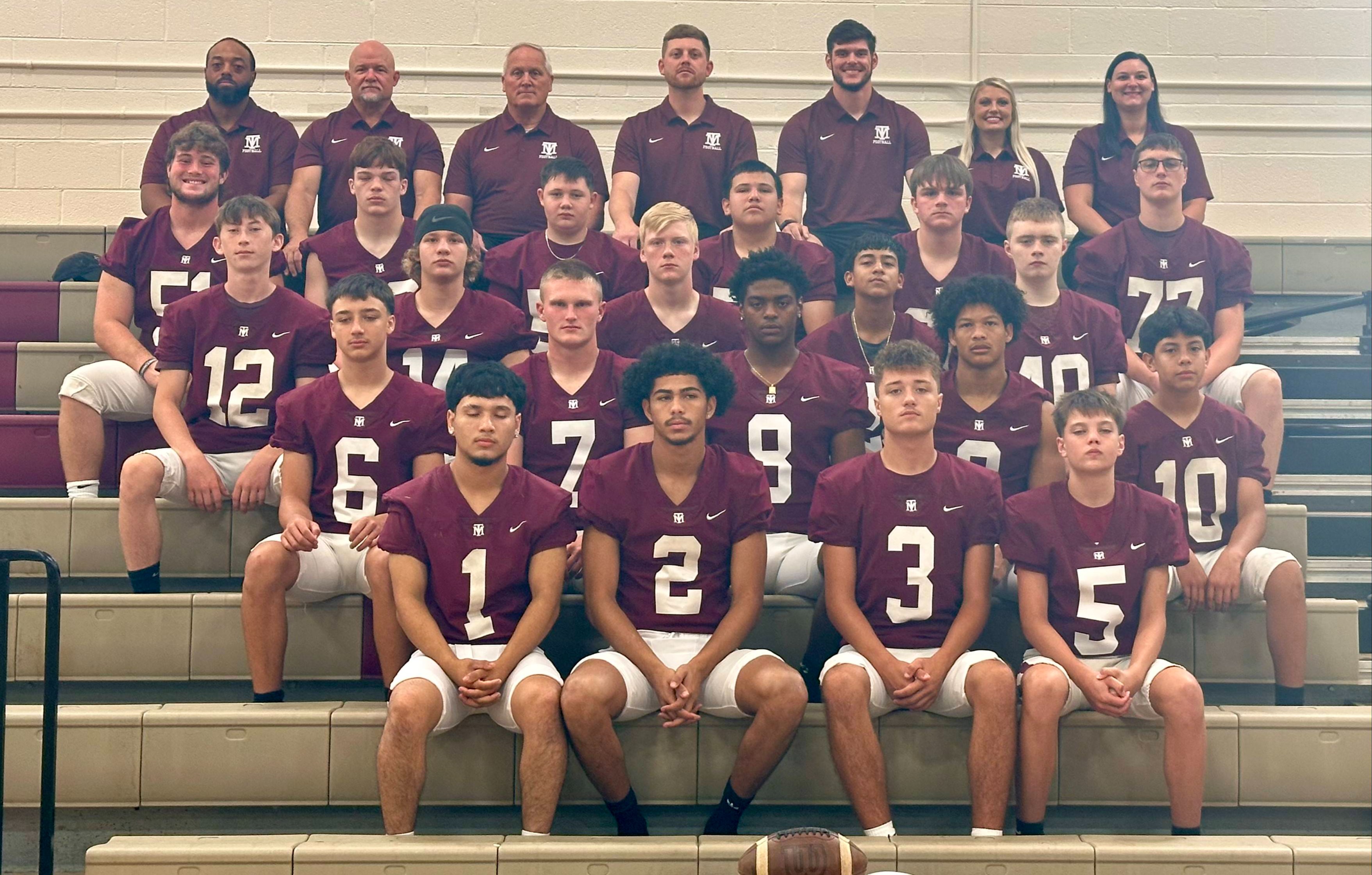 A high school football team in maroon uniforms pose on bleachers with numbers 1 through 12 visible.