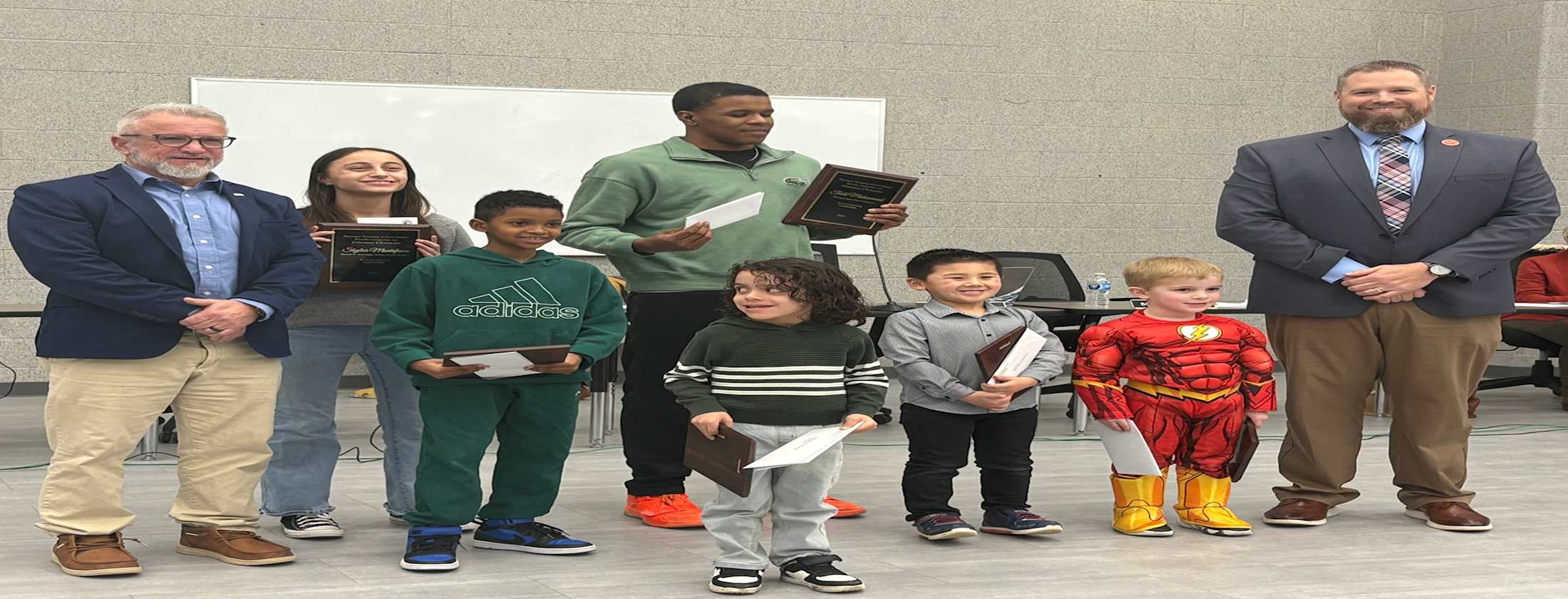 A diverse group of children and adults gathered in front of a podium, engaged and attentive to the speaker.