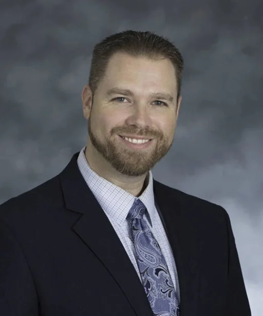 A man with a beard wearing a blue tie, exuding professionalism and confidence in his appearance.