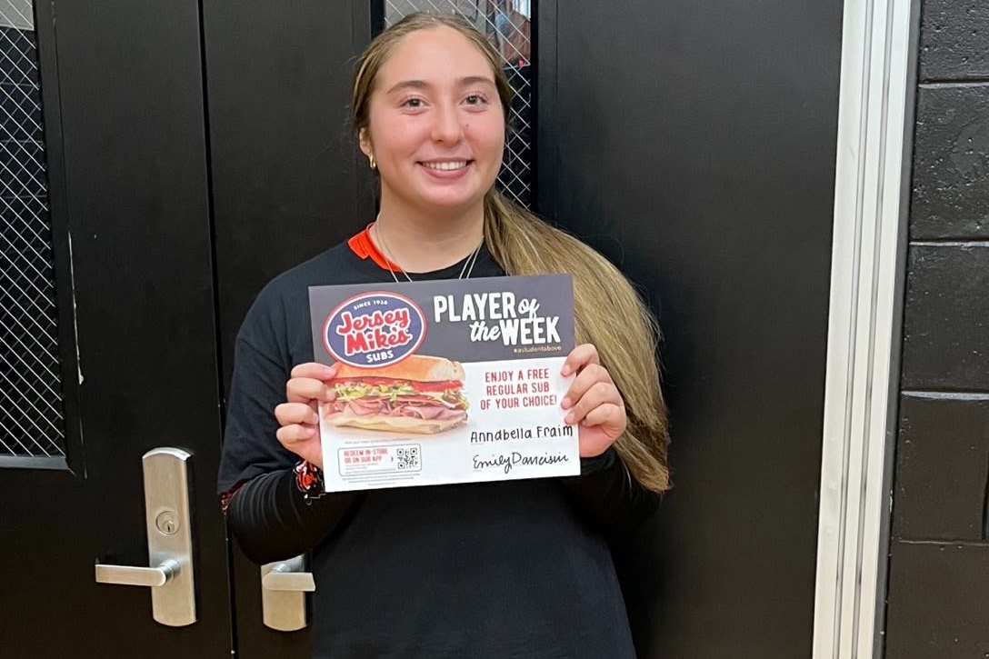 A girl stands smiling, holding a sign that reads "pizza," showcasing her enthusiasm for the delicious food.