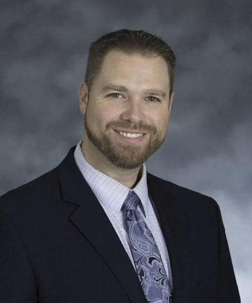 A man with a beard wearing a blue tie, exuding professionalism and confidence in a formal setting.
