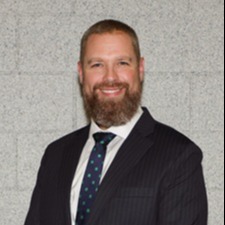 A man with a beard wearing a blue tie, exuding professionalism and confidence in his appearance.