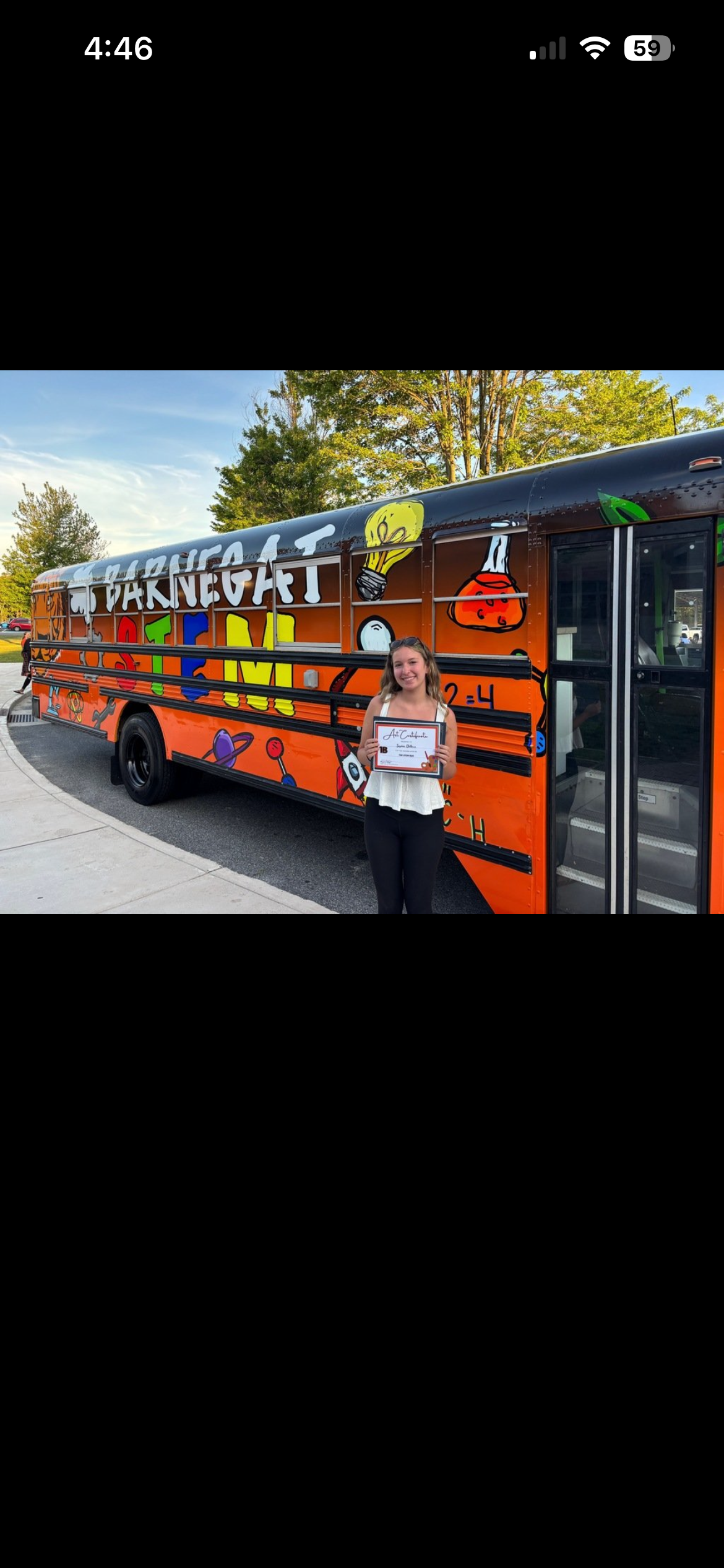 The student who designed the STEM bus stands in front of it with a certificate