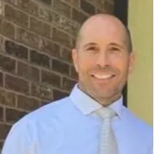 A man in a shirt and tie, exuding professionalism, friendliness, and confidence in his appearance.