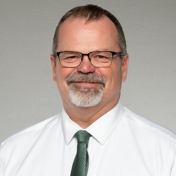 A man in a suit and tie poses for a professional headshot against a blue background.