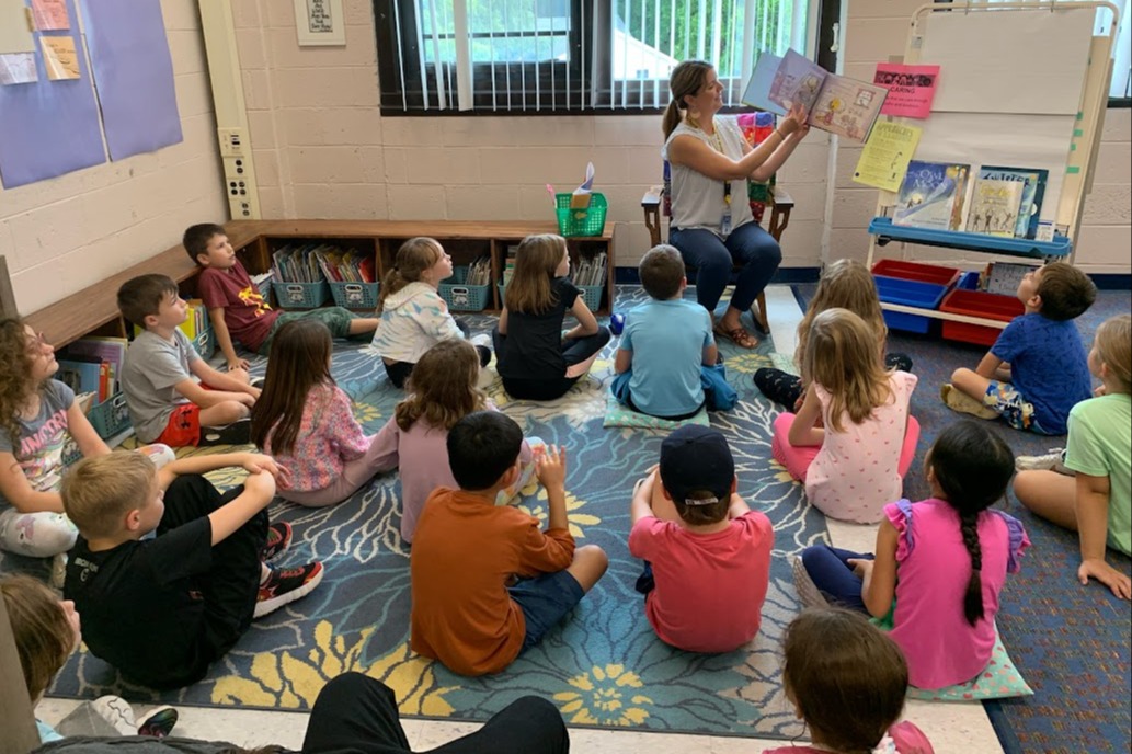 students on a rug listening to teacher read book