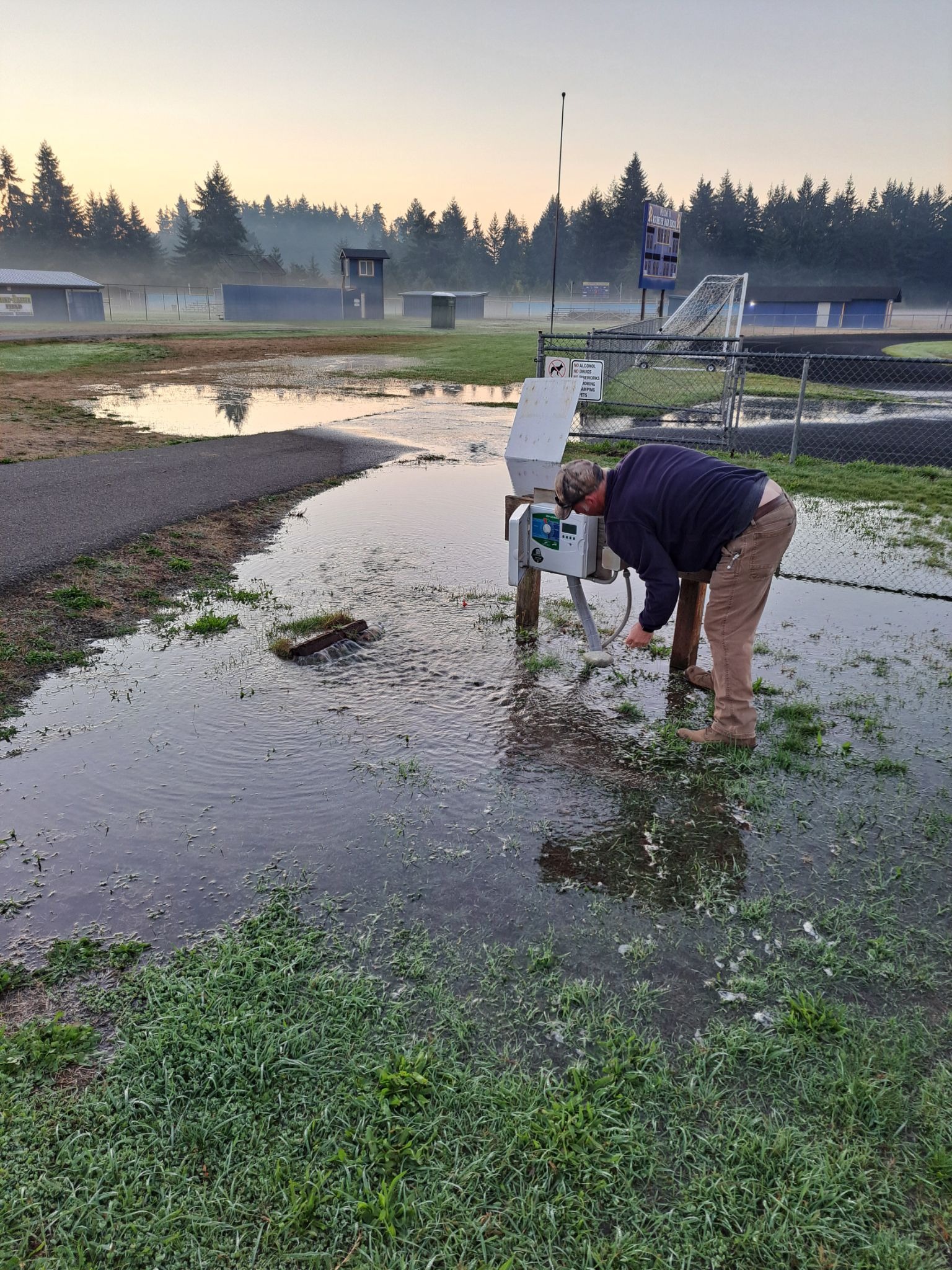 Person in blue shirt and tan pants inspecting water level near a parking lot.