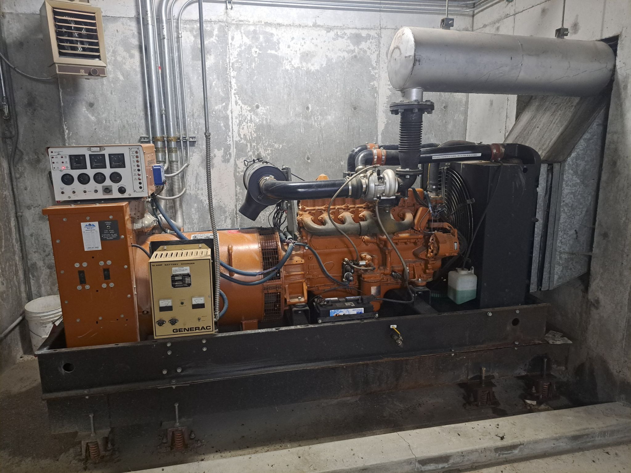 Industrial generator in a concrete basement. Multiple control panels and pipes are attached to the machinery.