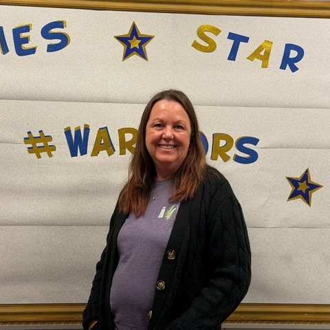 Woman stands in front of a white board with "Games Star # Warriors" and stars on it.
