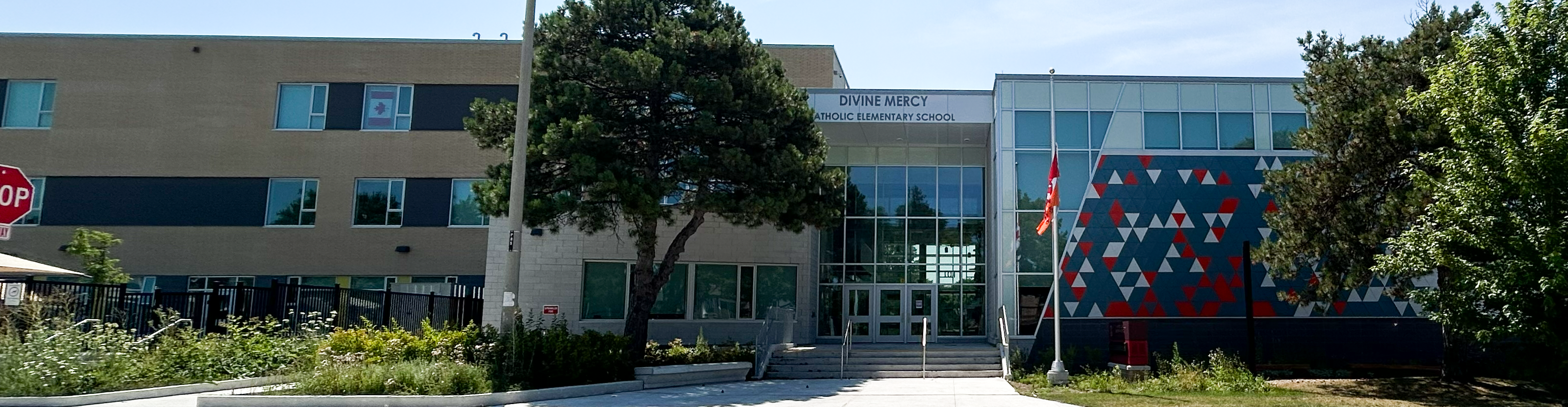 Photo of the Divine Mercy Catholic Elementary School building, showing the white and beige school building with trees and greenery in front, looking out onto a residential avenue