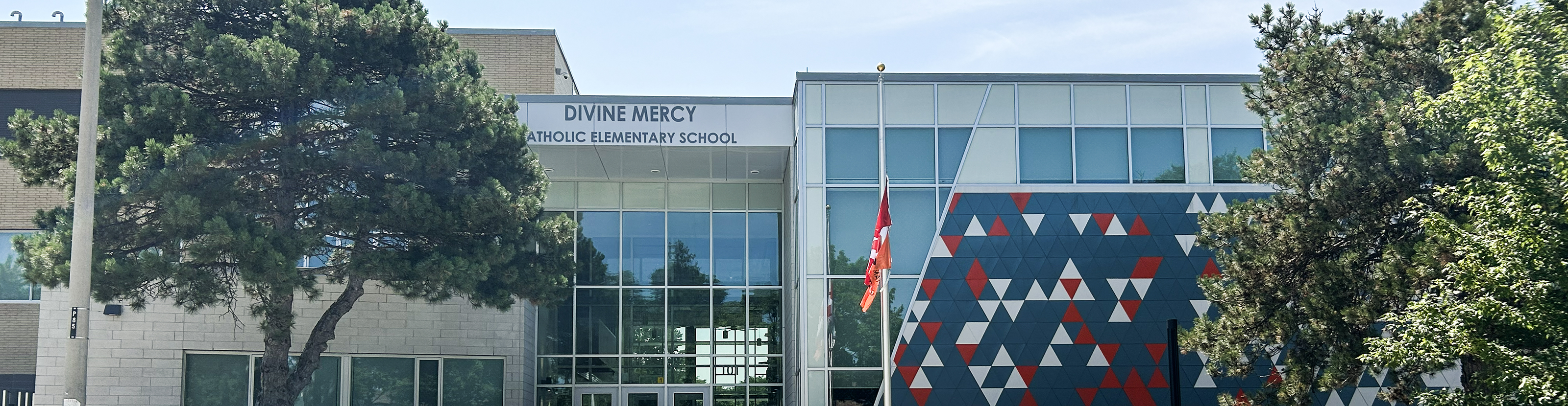 Photo of the Divine Mercy Catholic Elementary School building, showing the white and beige school building with trees and greenery in front, looking out onto a residential avenue