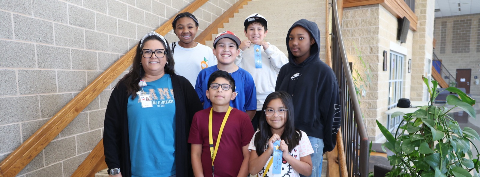 A group of six smiling students and teacher posing for the camera while some students showcase their ribbon.