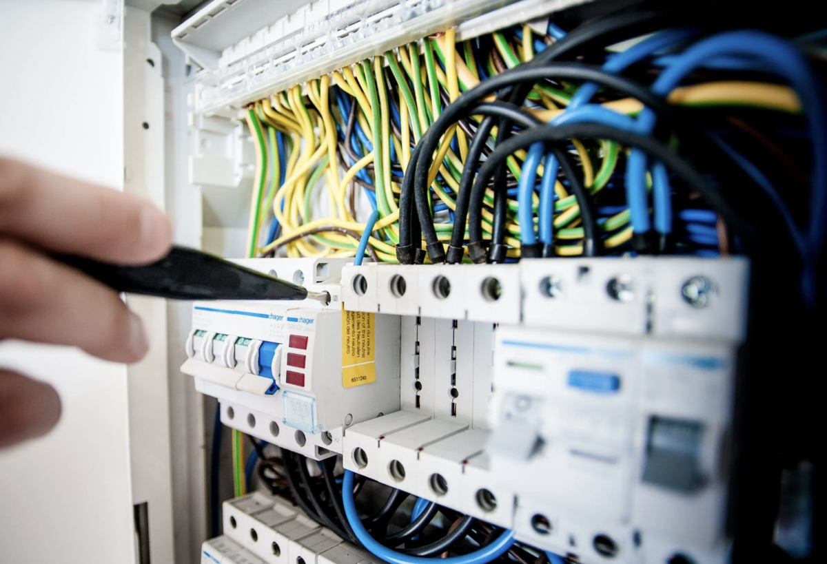 A close-up view of a person using a tool to work on a circuit breaker panel filled with colorful wires and electrical components.