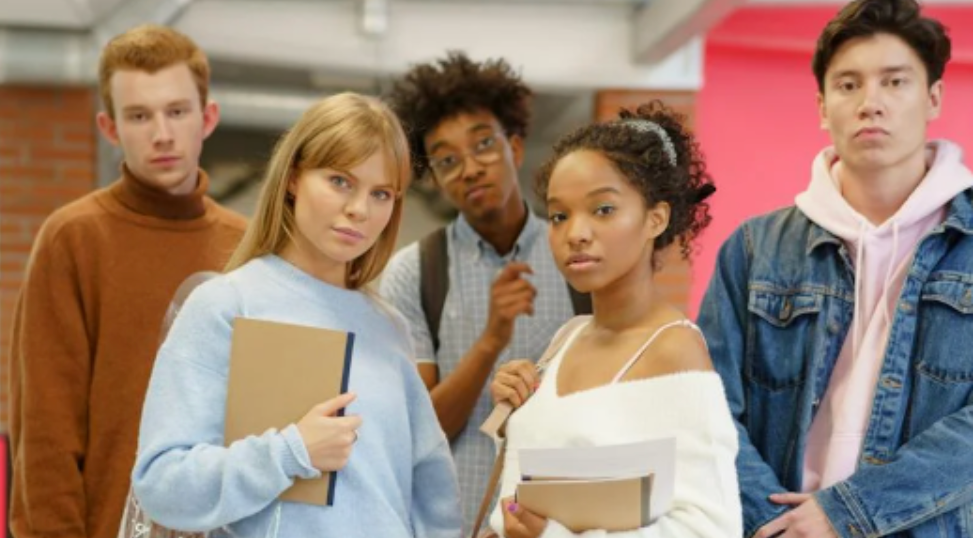 A group of high school students stands facing the camera in a school building.