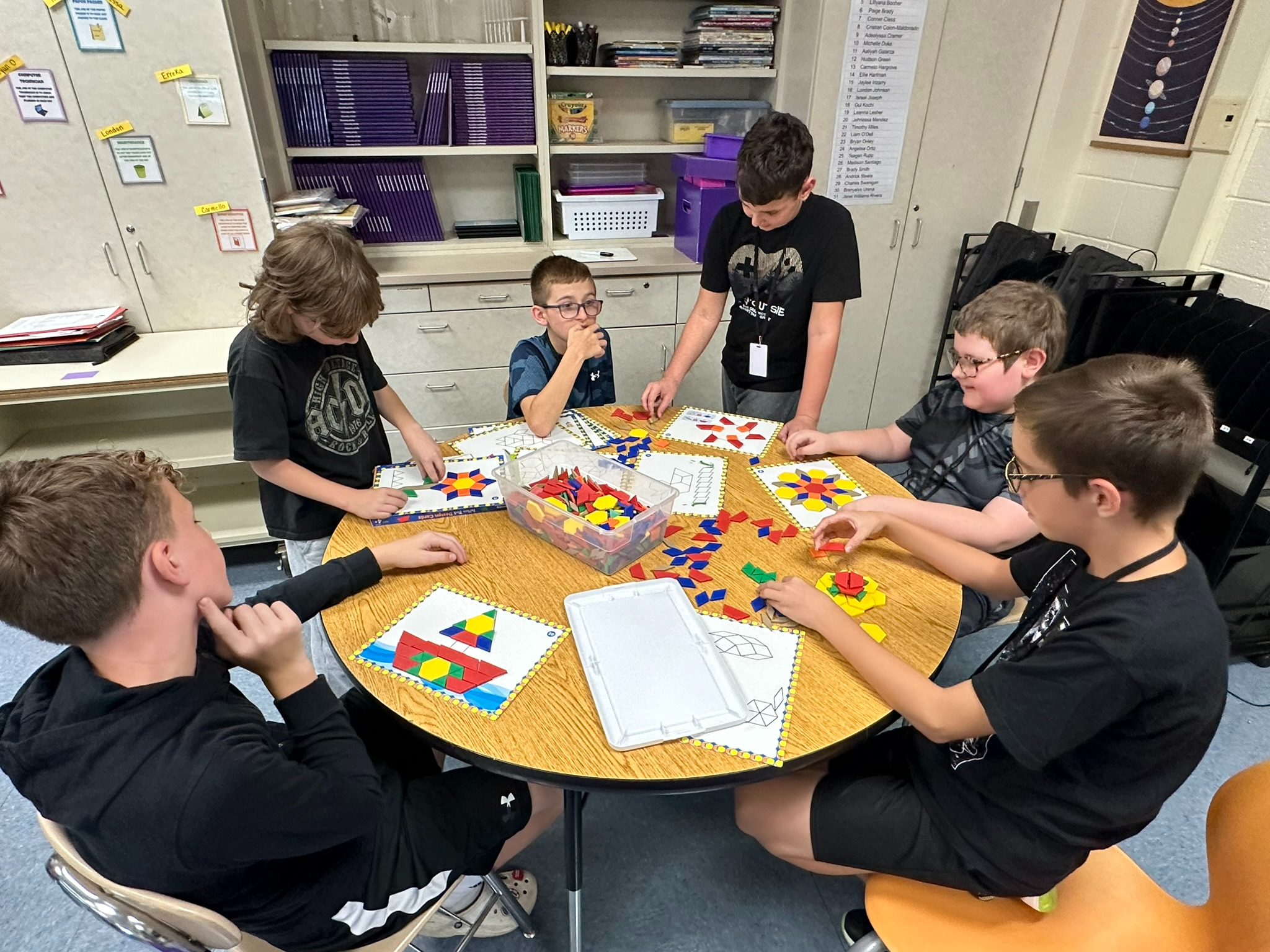 Six students sitting at a classroom table working on classwork together