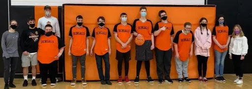 A group of students wearing orange "Bengals" jerseys and masks poses in a gym, holding a basketball against an orange backdrop.