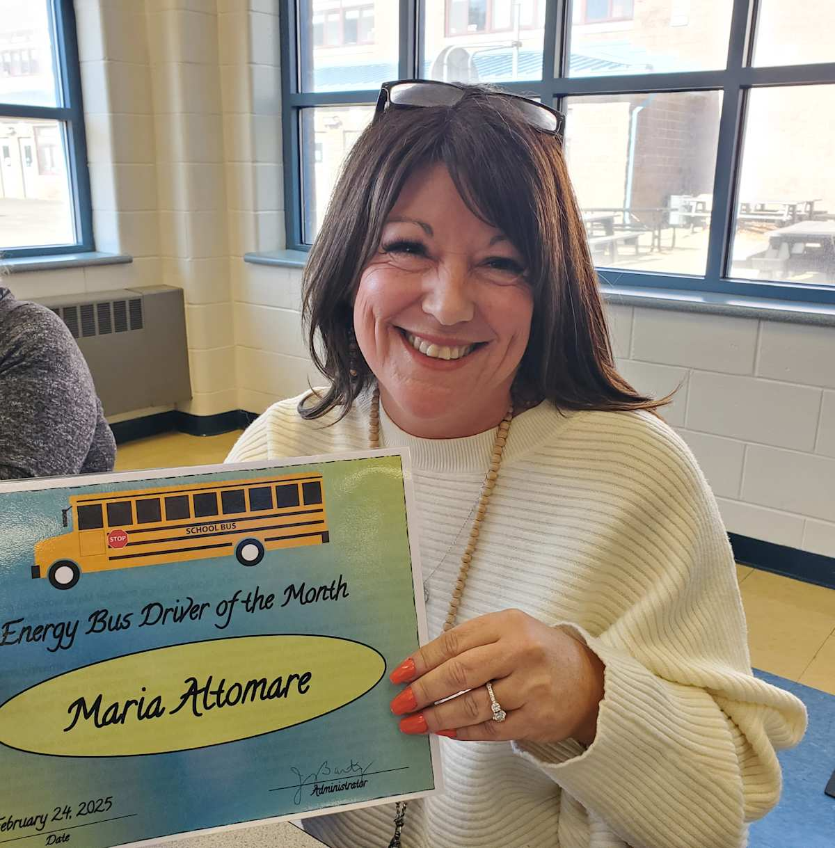 A woman proudly displays a certificate recognizing her achievements as a bus driver.