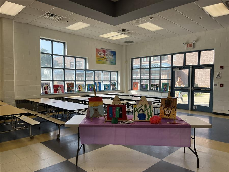 A classroom featuring tables, chairs, and colorful paintings adorning the walls, creating an engaging learning environment.