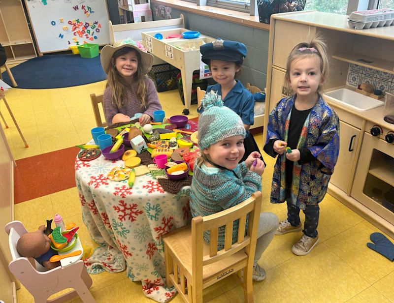 Three children seated at a classroom table, engaged in an activity together, surrounded by educational materials.