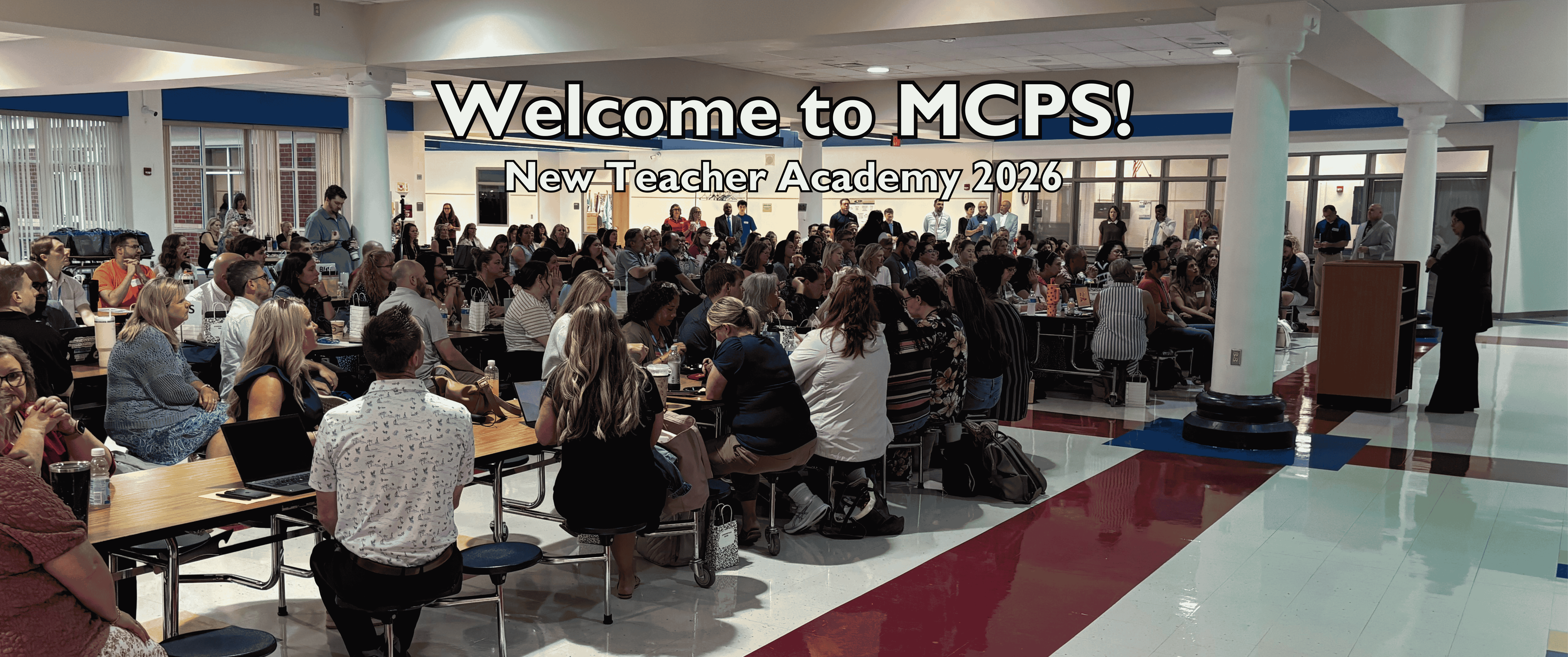 Room of people sitting at tables with text saying "Welcome to MCPS. New Teacher Academy 2026"