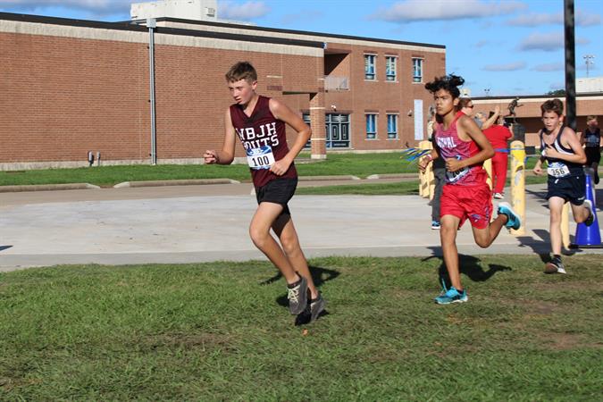 A group of young runners competing in a cross-country race on a grassy field near a school building.