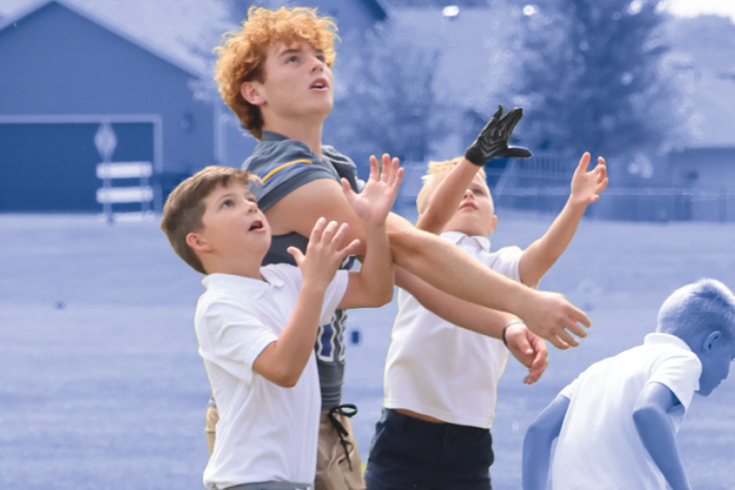 high school football player playing with elementary students