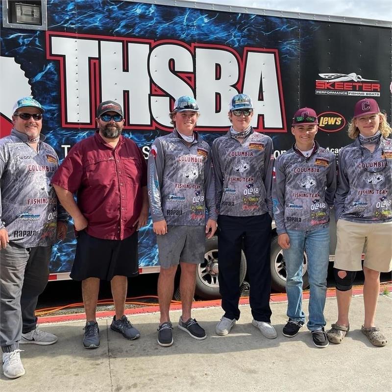 A group of six individuals, wearing matching fishing jerseys and caps, stand in front of a trailer displaying the logo 'THSBA'.