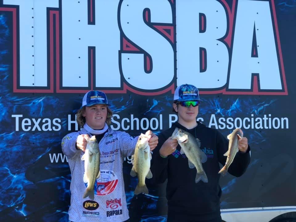 Two young anglers proudly display their catches of bass in front of a banner for the Texas High School Bass Association.