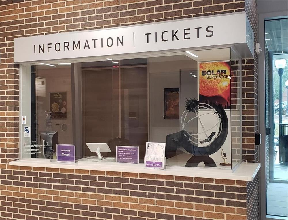 A ticket and information counter with a sign above reading 'INFORMATION | TICKETS', featuring a promotional poster for a solar exhibit and a clean, modern design.