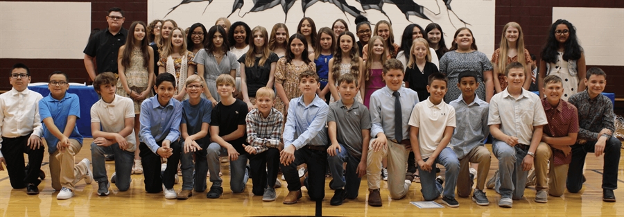 A large group of students, both boys and girls, are posing together for a photo in a school setting, with a mural in the background.