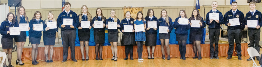 A group of students in blue jackets stands in a line, each holding a certificate, in a formal indoor setting with a decorative background.