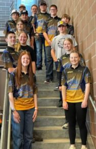 A group of young people wearing matching team shirts stands on a staircase, smiling at the camera.
