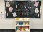 A bulletin board displaying the phrase 'Oh, the places you'll go - Dr. Seuss' with colorful letters, surrounded by various educational posters, and a wooden shelf filled with children's books below.