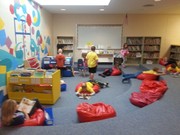 A colorful children's reading area featuring bean bag chairs, a bookshelf, and children engaged in various activities, including reading and playing.