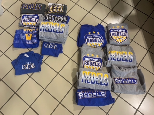 A collection of various t-shirts and sweatshirts displaying the word 'REBELS' in different colors and styles, arranged neatly on a tiled floor.