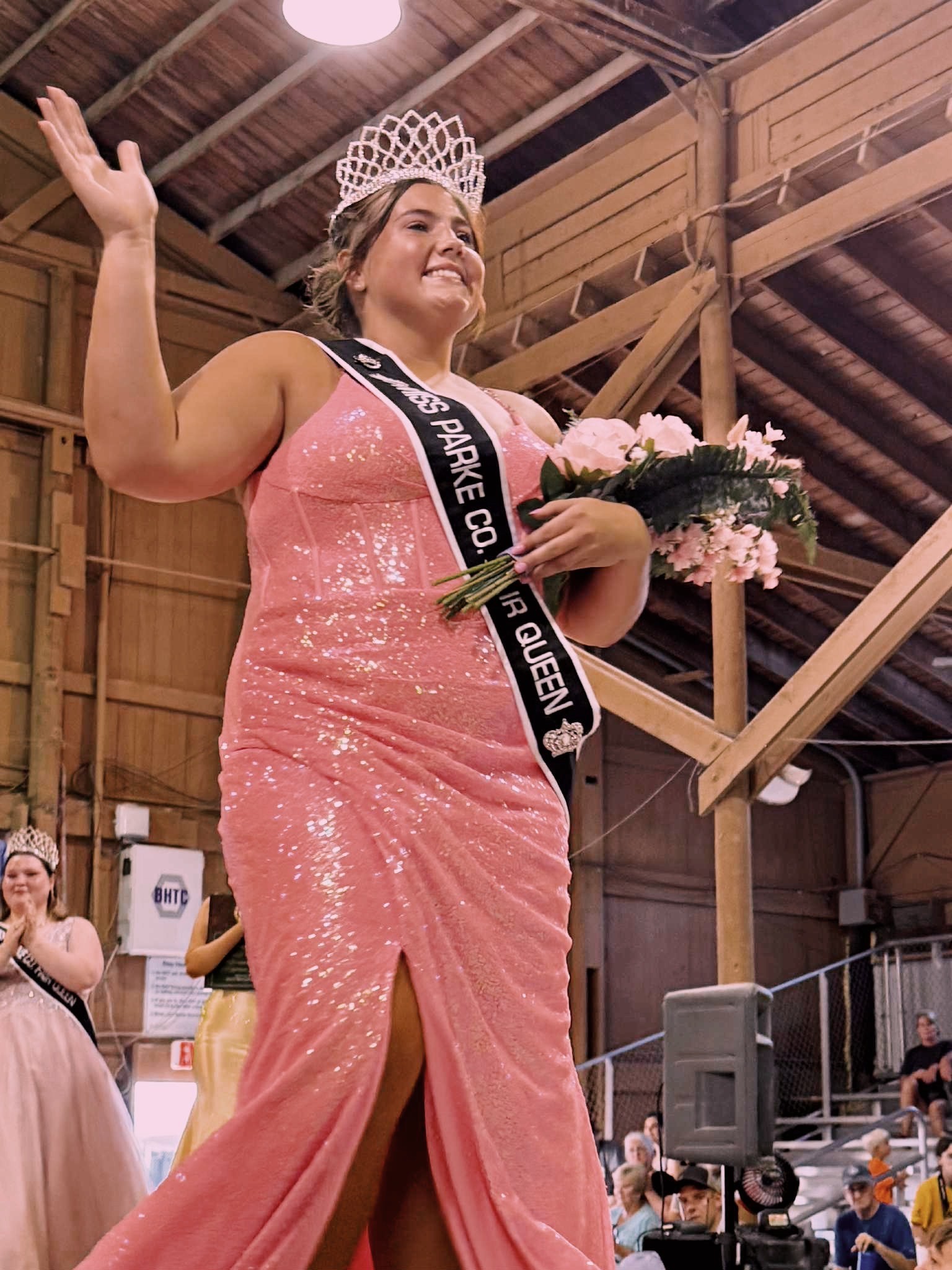 girl wearing a sash and holding flowers and waving to the audience