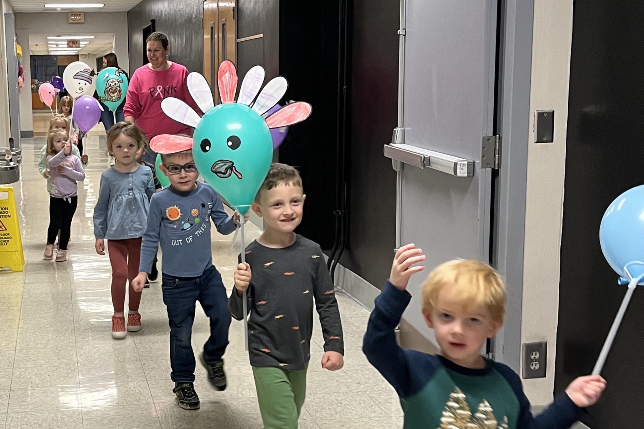 preschool students walking through a hallway holding balloons