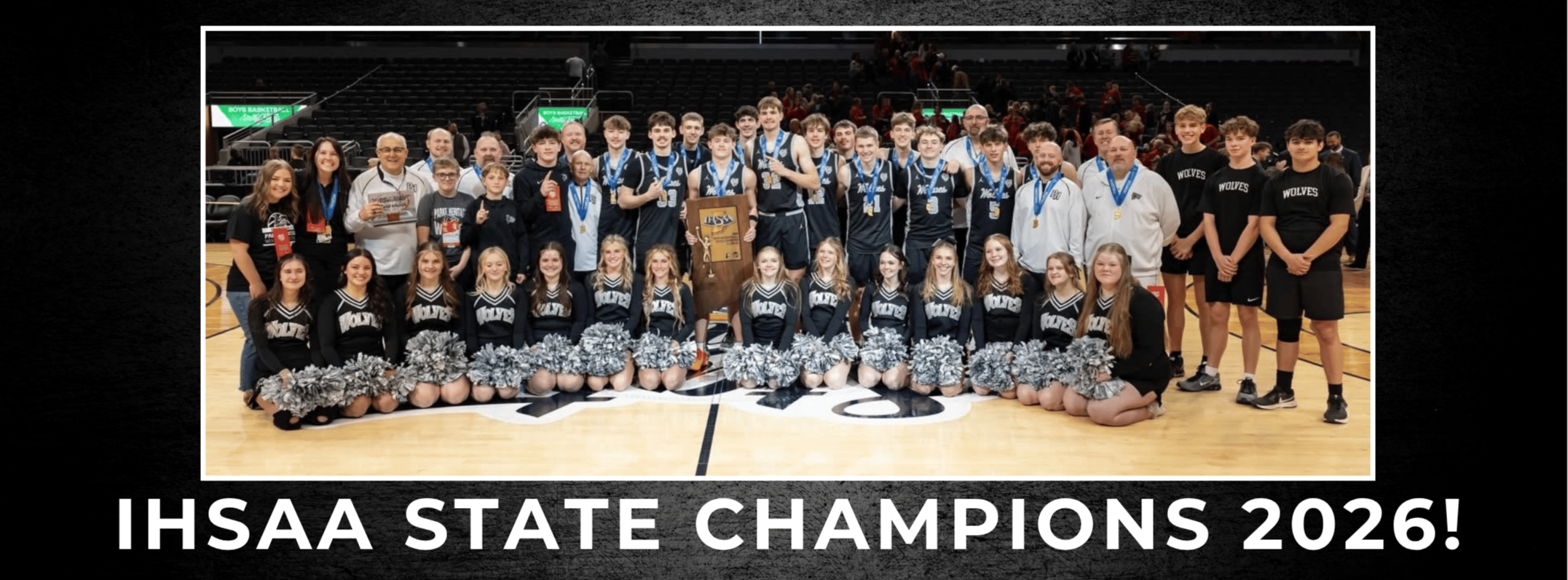 Group photo of a boys’ basketball team, cheerleaders, coaches, staff, and supporters posing on a basketball court with a championship trophy and medals. Large text below the photo reads, “IHSAA STATE CHAMPIONS!”