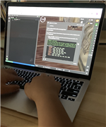 A person is typing on a laptop keyboard, with a programming interface displayed on the screen showing code and a game-like environment.