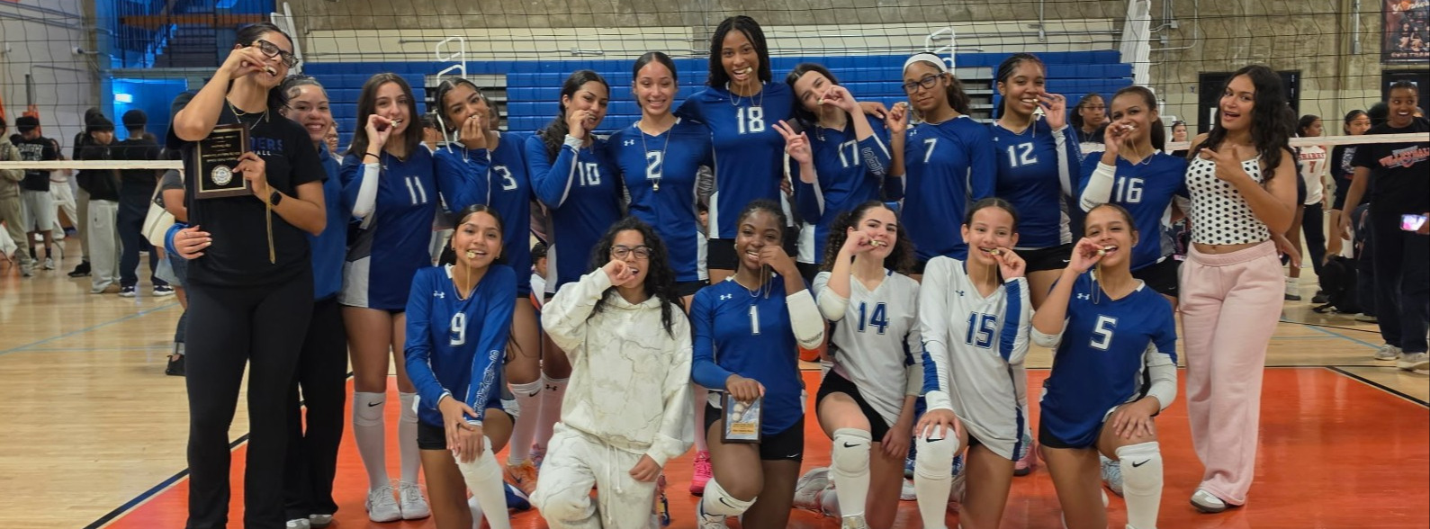 Members of the Citywide Volleyball Tournament championship team pose together on the gym court in blue and white uniforms, displaying their medals and award plaque.