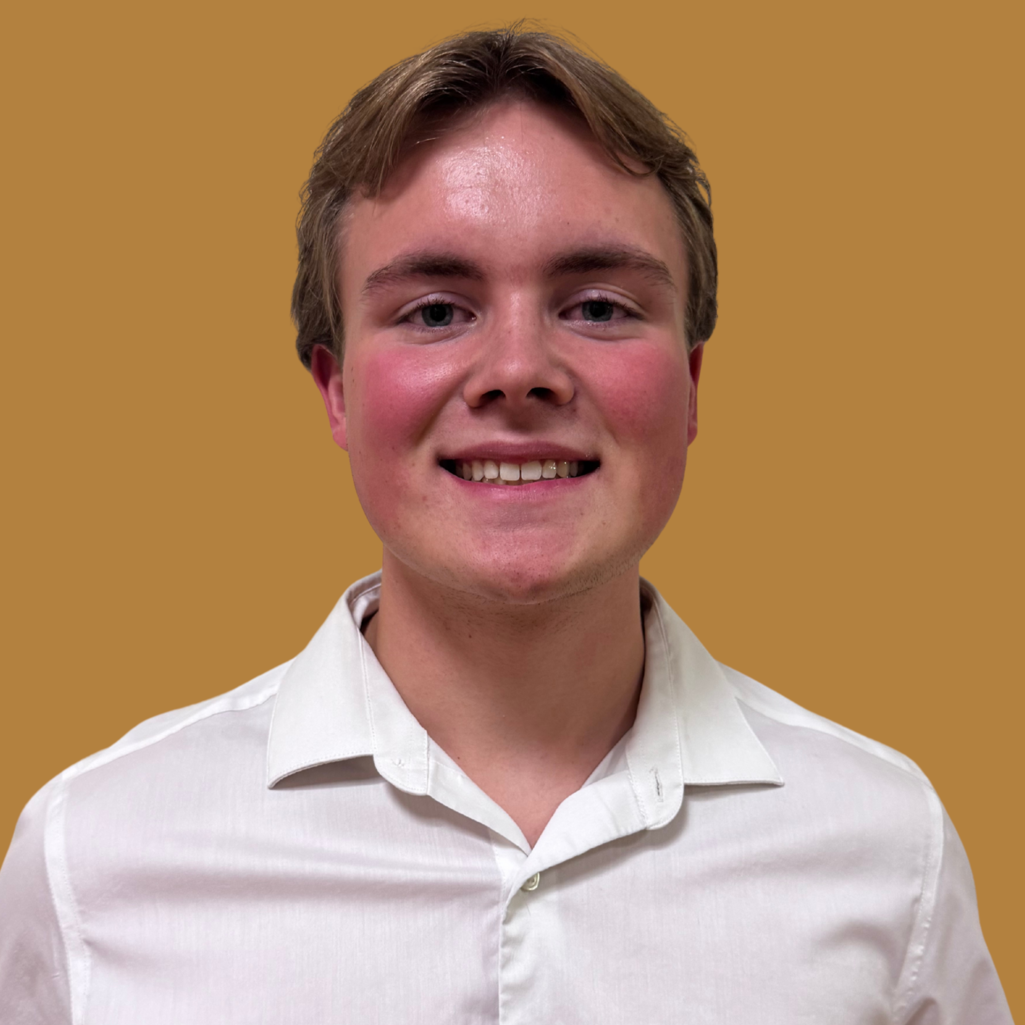 A man smiles in front of a bright yellow background. He wears a white shirt with a collar and buttons.