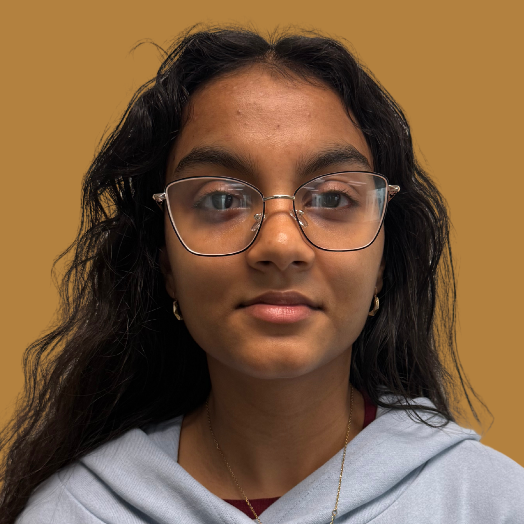 Woman with black hair, glasses, and a gray hoodie featuring a Snoopy graphic, set against a brown background.