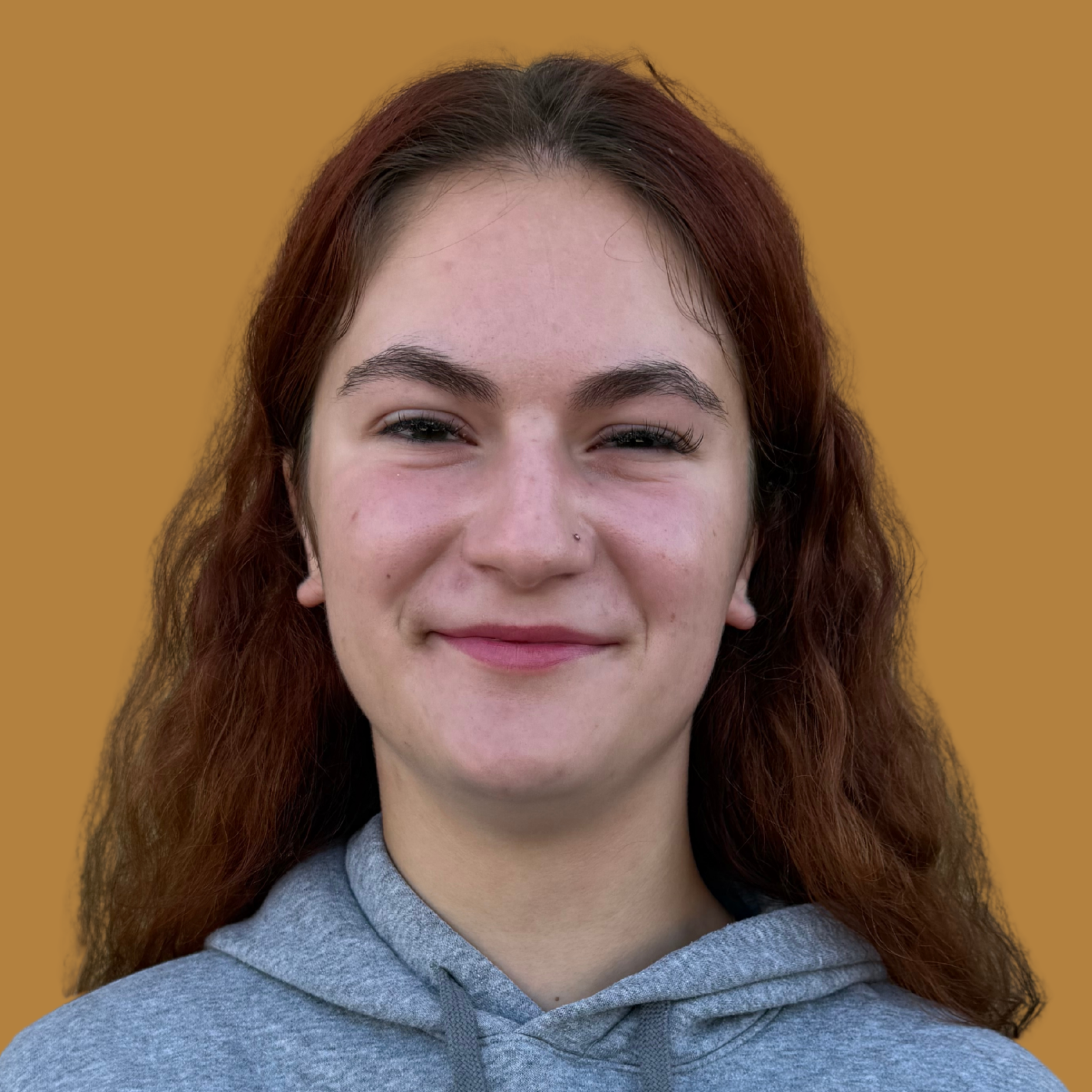 A woman with brown wavy hair smiles. She wears a grey hoodie with "WOLVES" printed in dark blue.